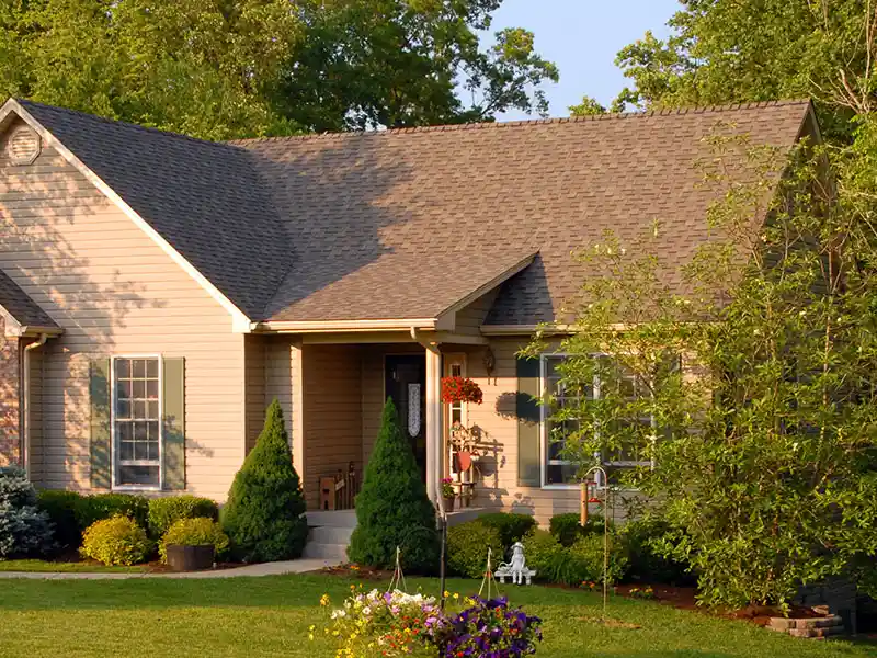Small tan home surrounded by tress and plants