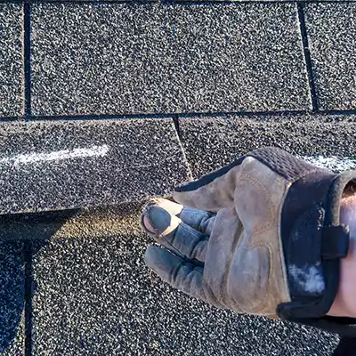 Close up of a gloved hand lifting and inspecting underneath a roof shingle